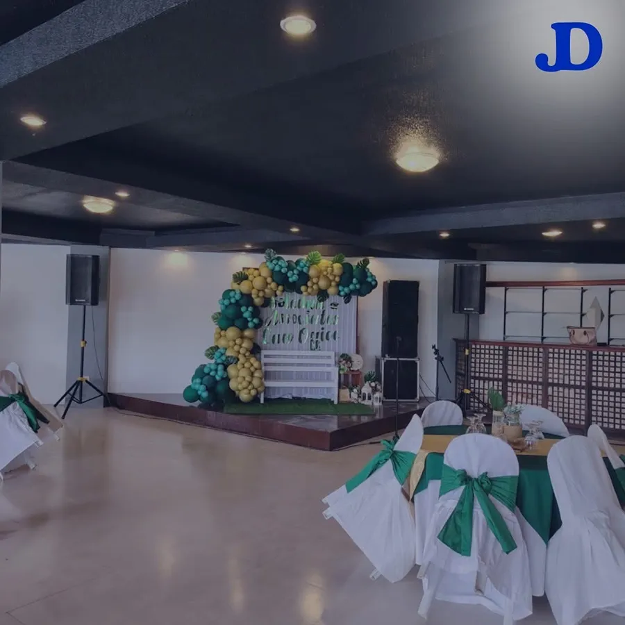 Reception hall with a balloon garland stage backdrop and PA speakers on stands under warm ceiling lighting