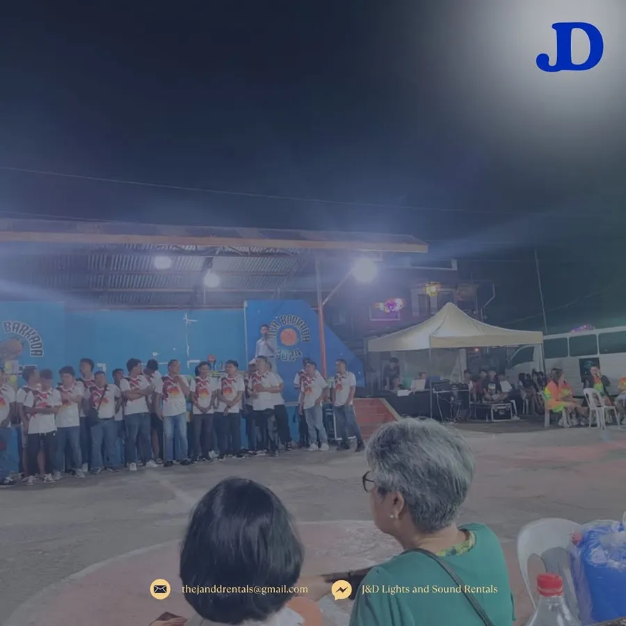 Evening stage with a lineup of participants in matching shirts, crowd seated under a tent